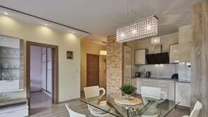 A modern dining area with a glass table, white chairs, and a decorative plant centerpiece. - Apartamenty Swinoujscie-Wojska Polskiego (Swinoujscie)