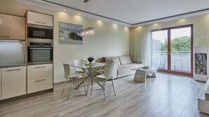 A modern kitchen with built-in appliances, a dining area with a glass table, and a balcony with a view. - Apartamenty Swinoujscie-Wojska Polskiego (Swinoujscie)