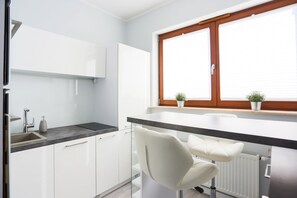 A modern kitchen with white cabinets, a black countertop, and a window with blinds.
