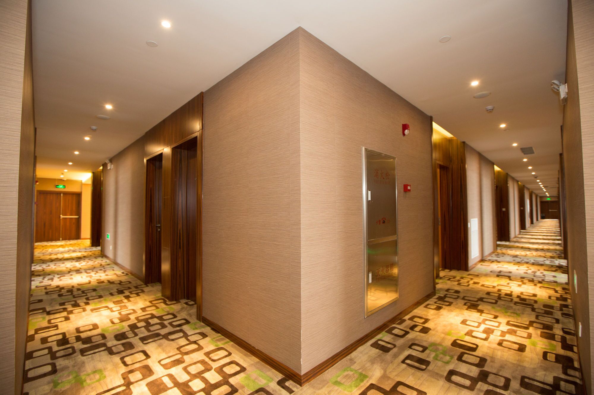 Ein Hotelgang mit einem gemusterten Teppich, Holztüren und einer Spiegelwand.