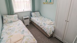 A bedroom with two single beds, a nightstand, a wardrobe, and a window with curtains. - Number 6 Oxwich Leisure Park (Swansea)