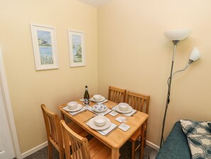 A dining area with a wooden table set for four, two framed pictures on the wall, and a floor lamp.