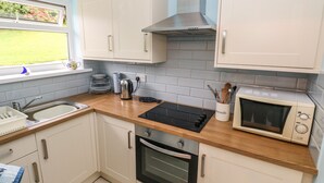 A modern kitchen with white cabinets, a black stove, a microwave, and a window with a view of greenery. - Number 6 Oxwich Leisure Park (Swansea)
