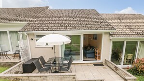 A patio with a table and chairs, a white umbrella, and a glass door leading to an interior space. - Number 6 Oxwich Leisure Park (Swansea)