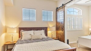 Une chambre à coucher avec un lit en bois, deux lampes de chevet, une grande fenêtre avec des stores et une porte coulissante de style grange.