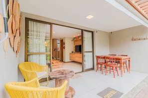 A modern interior with a dining area, yellow wicker chairs, a wooden table, and a kitchen visible through a glass door.
