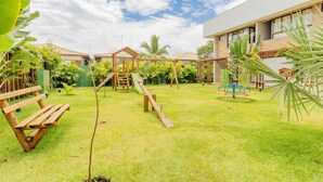 A playground with swings and slides, surrounded by greenery and a building. - IT29 Excelente ap 3 Quartos 50m da Praia (Camaçari)