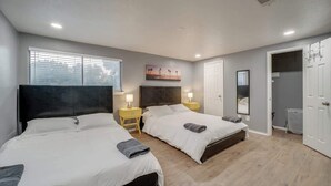 A bedroom with two beds, a large window, and a door leading to a bathroom. - Modern 5BR w/ Pool, Cinema & Game Room (Dallas)
