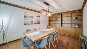 A dining area with a wooden table, blue chairs, a chandelier, and a bookshelf. - Modern 5BR w/ Pool, Cinema & Game Room (Dallas)