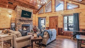 L’intérieur chaleureux d’un chalet avec une cheminée en pierre, des murs en bois et un plafond haut avec des poutres apparentes.