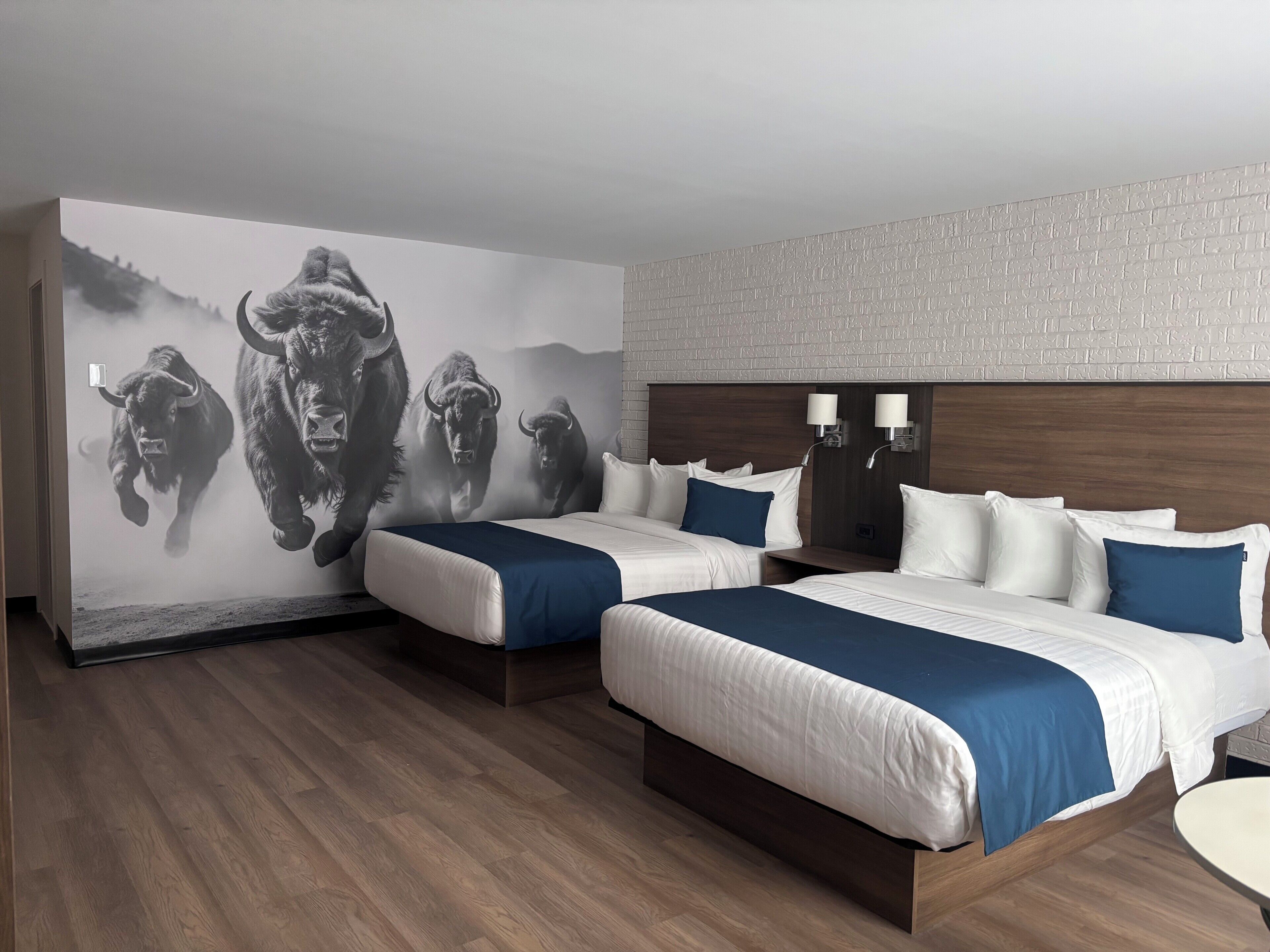 A hotel room with two beds, a large wall mural, a brick-patterned wall, and a wooden floor.
