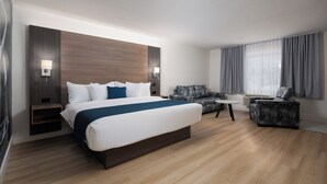 Habitación de hotel con una cama grande, un sofá, una mesita y un televisor de pared.