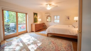 Une chambre comprenant un lit, une commode, un ventilateur de plafond et une porte-fenêtre coulissante donnant sur un espace extérieur avec une terrasse et des chaises.