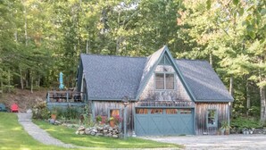 Une cabane rustique avec des fondations en pierre, une terrasse en bois et un garage.