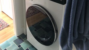 A front-loading washing machine and dryer in a laundry room with a patterned rug on the floor.