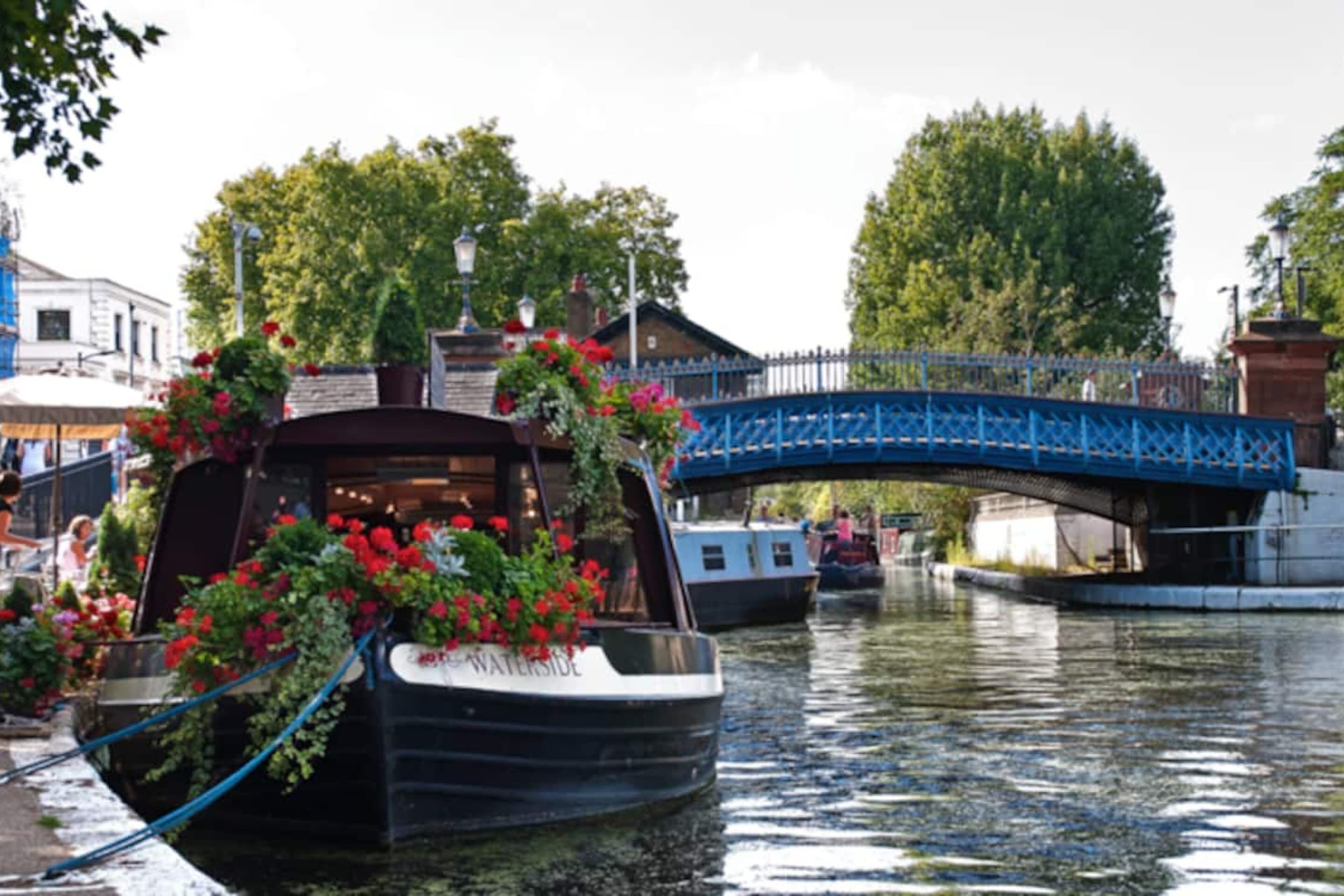 A boat docked at a canal with a blue bridge in the background.