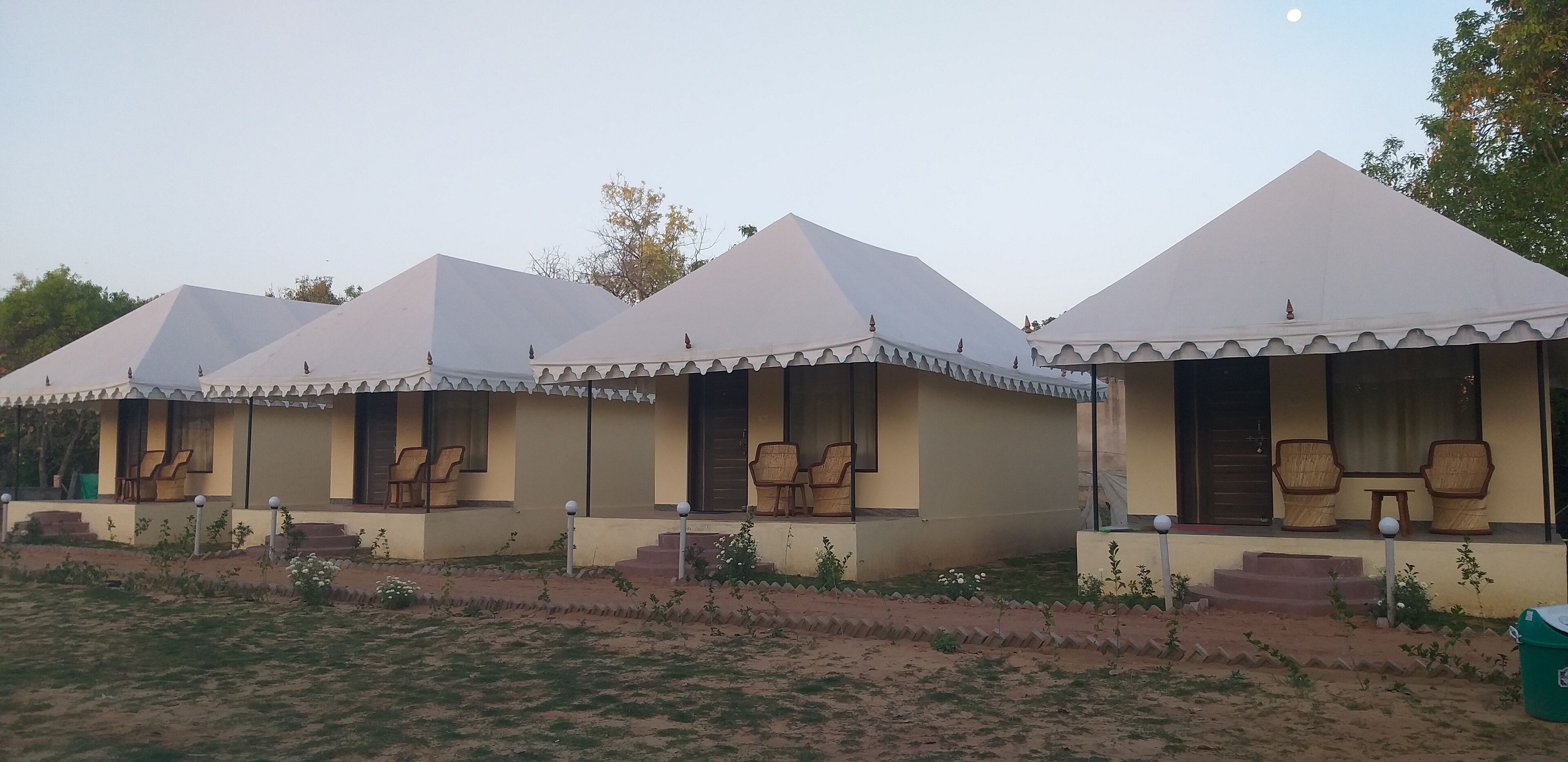 A row of small, single-story buildings with conical roofs and a porch area with chairs.
