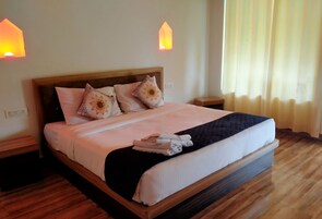 Una cama bien hecha con almohadas, una toalla doblada y un cabecero de madera. Hay dos mesitas de noche con lámparas.