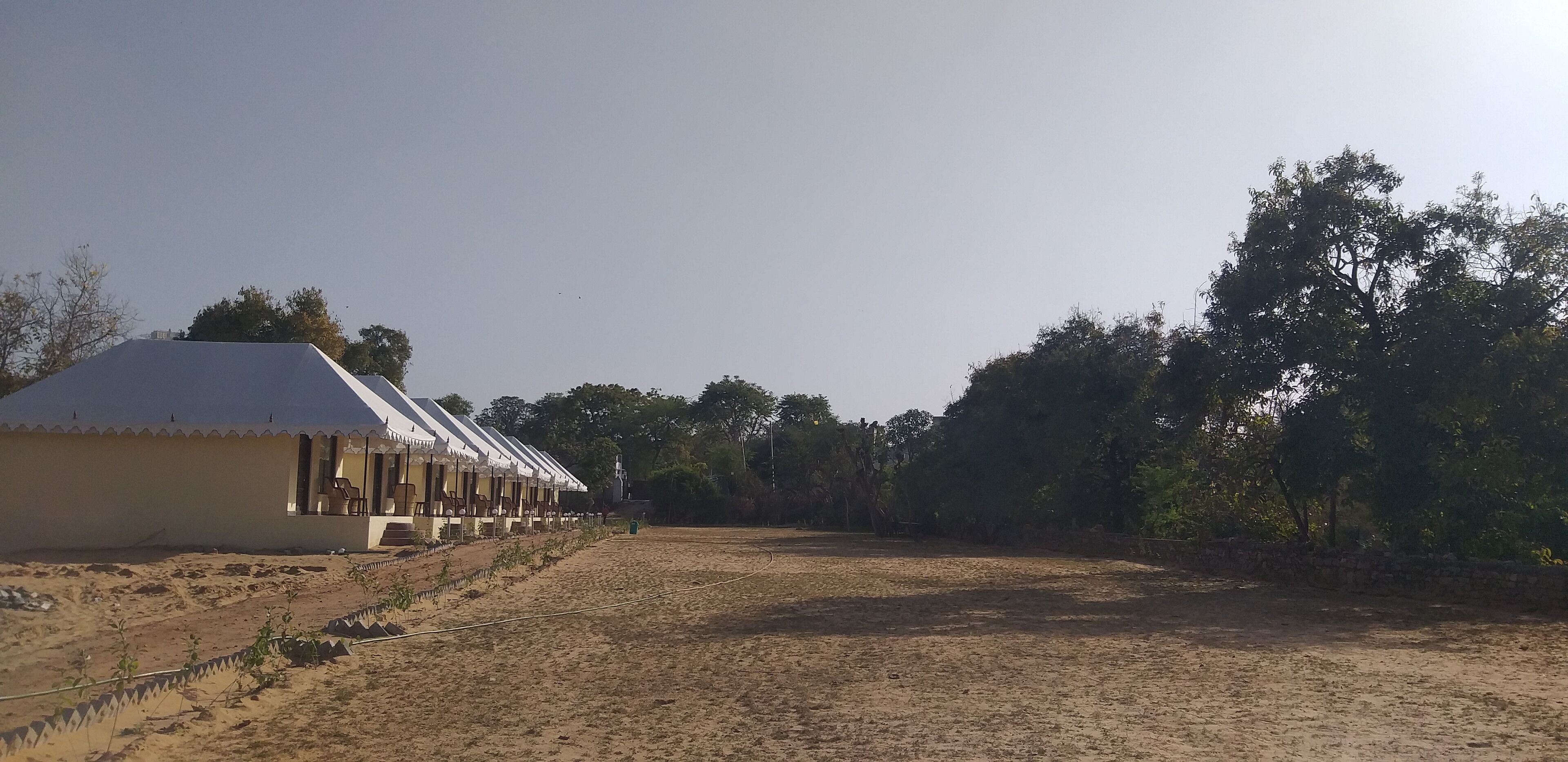 A row of single-story buildings with a flat roof, likely a hostel or guesthouse, with a dirt ground in front.