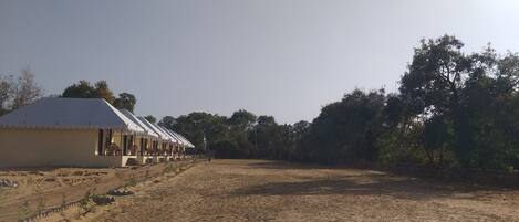 A row of single-story buildings with a flat roof, likely a hostel or guesthouse, with a dirt ground in front.