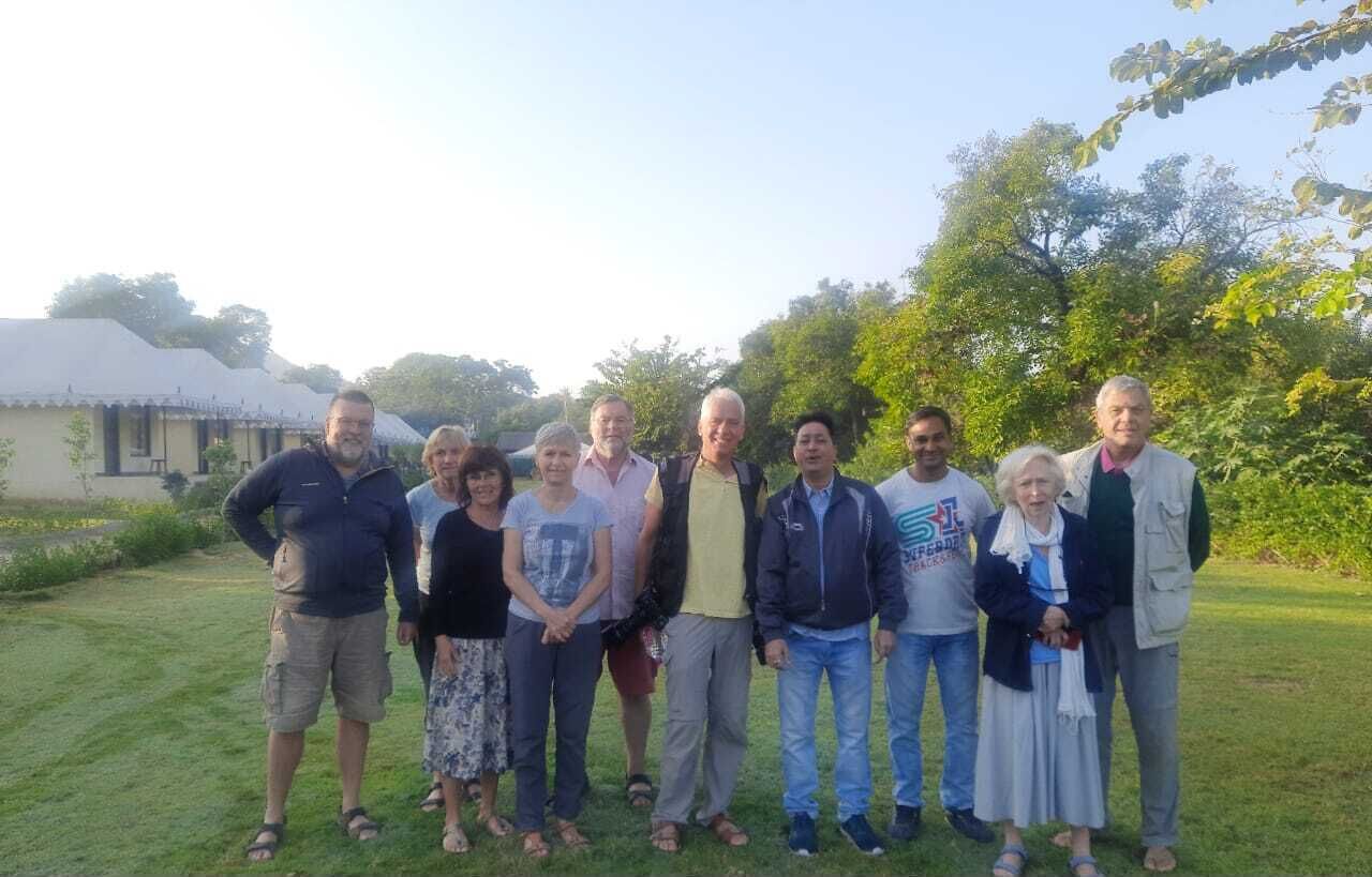Un grupo de personas de pie al aire libre en un área con césped, árboles y un edificio al fondo.
