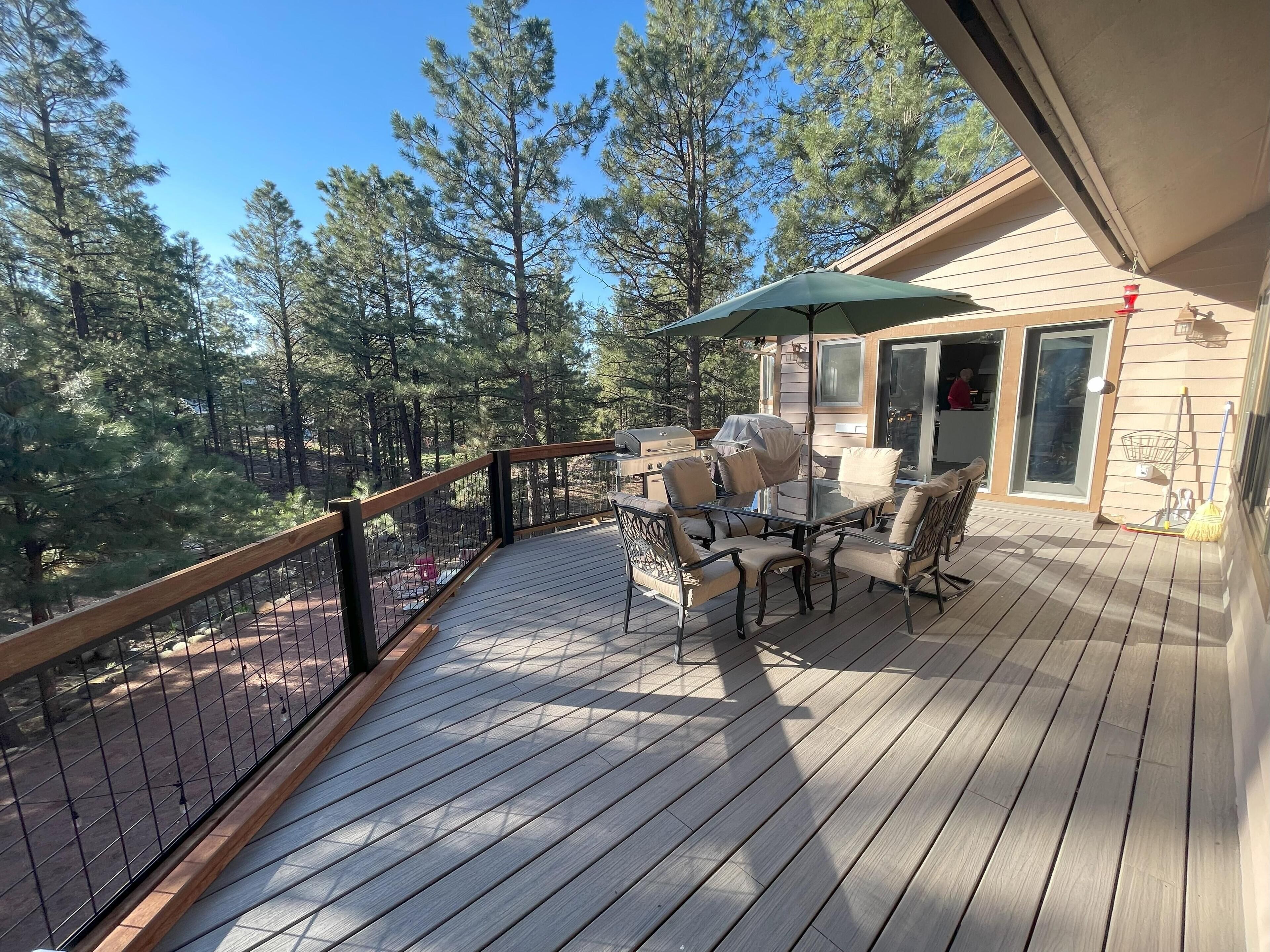 Una terraza de madera con mobiliario exterior, una mesa cubierta y vista a un bosque.