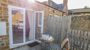 Une maison en pierre avec une clôture en bois, une porte-fenêtre coulissante et une petite table avec un service à thé.