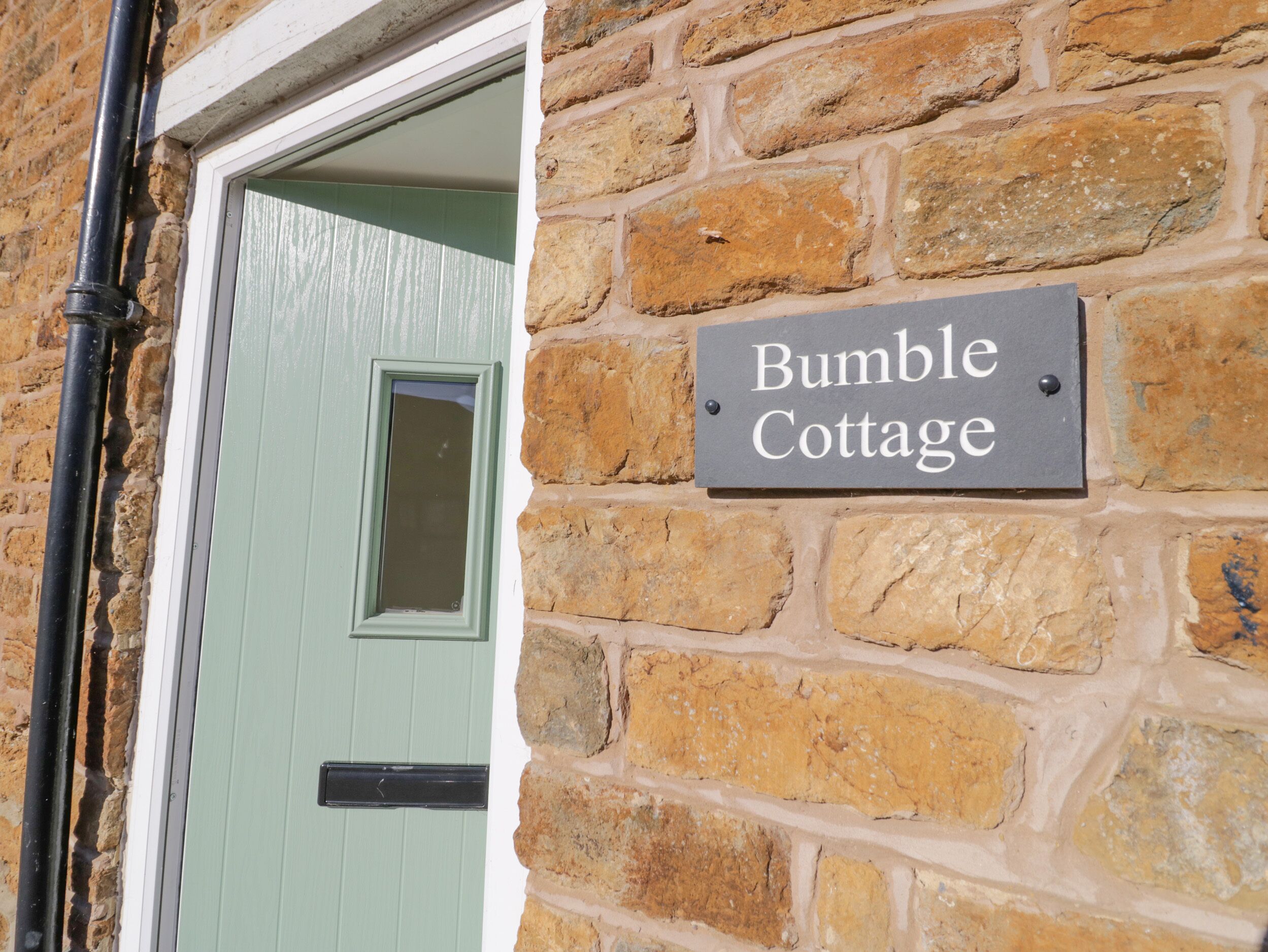 Un muro de piedra con un letrero que dice "Bumble Cottage".