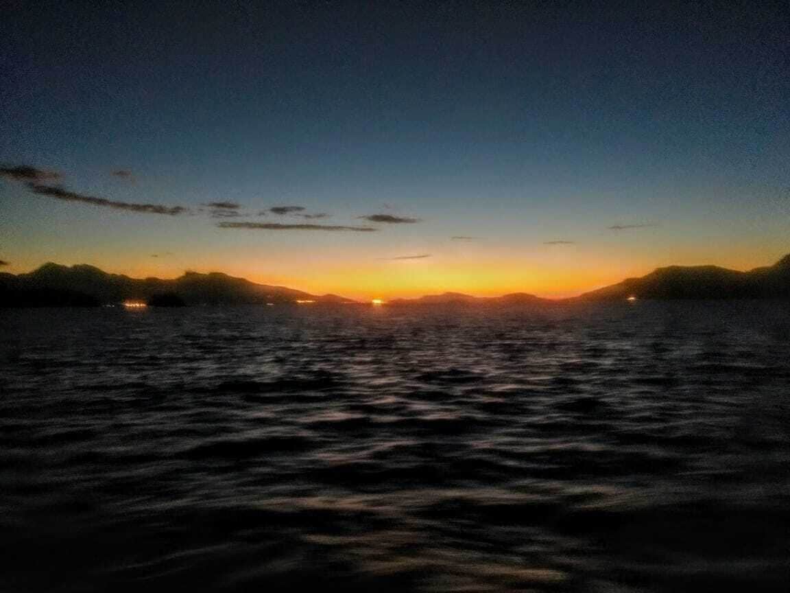 Un coucher de soleil sur une étendue d’eau, avec les silhouettes lointaines de terres sur l’horizon.