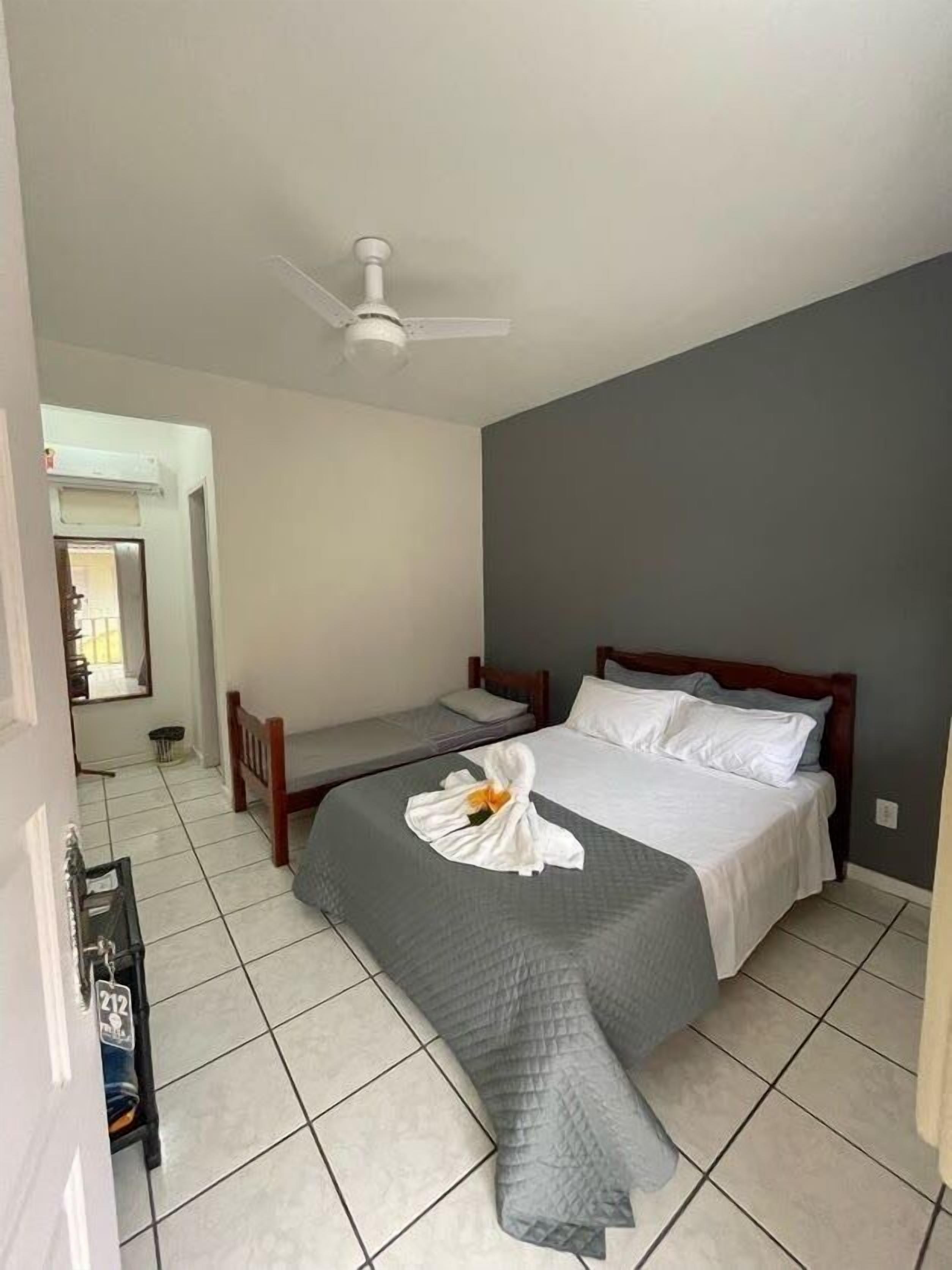 Una habitación de hotel con una cama, una cama adicional, un ventilador de techo y piso de baldosas.