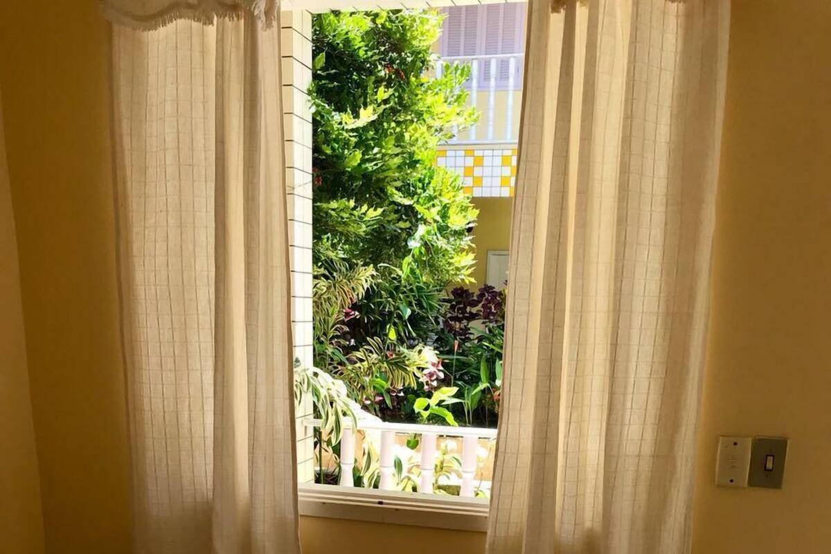 A bedroom with a bed, floral bedding, a view of greenery outside, and a window with curtains.