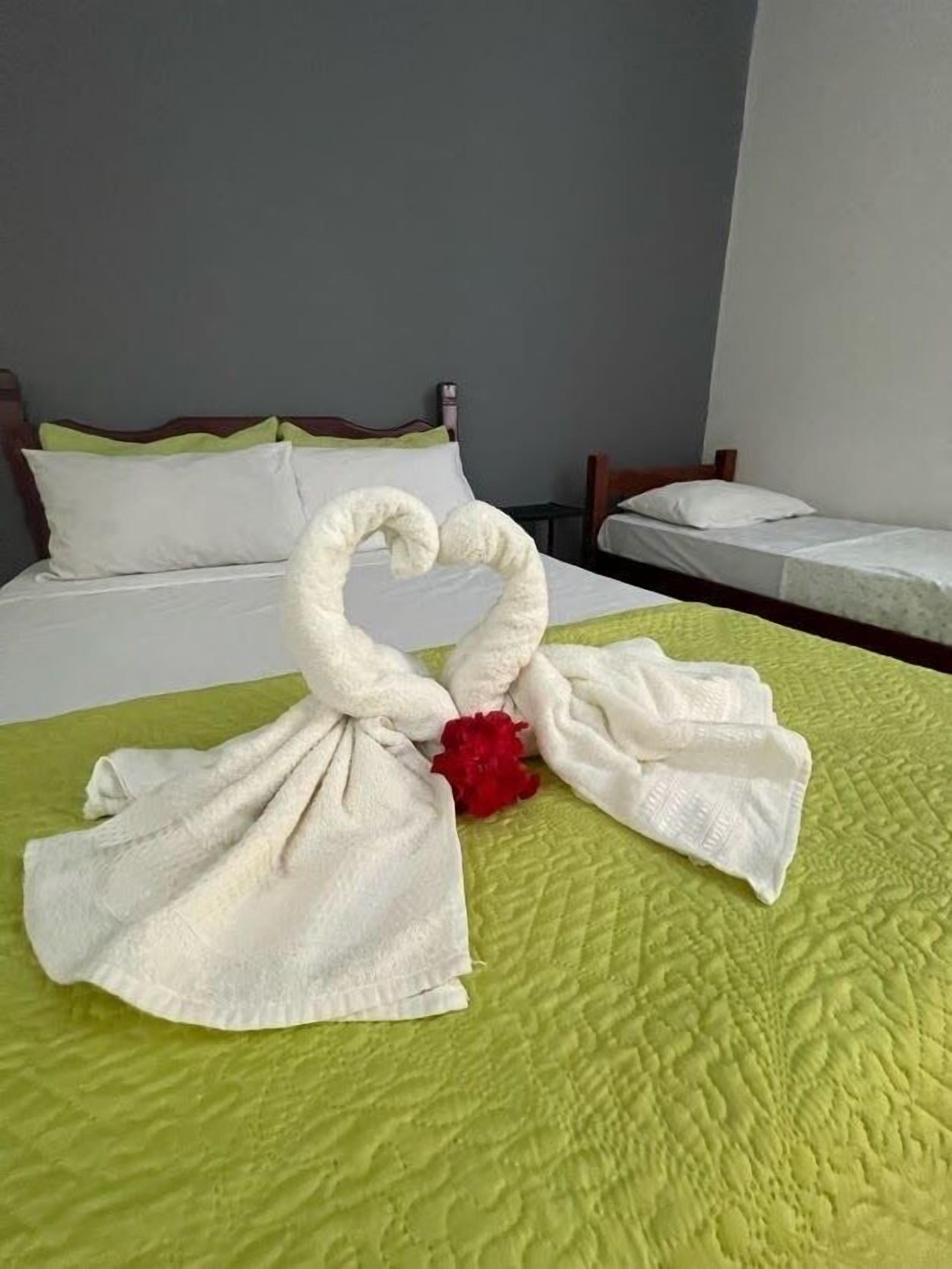 A hotel room with a bed, a smaller bed, and a decorative swan towel arrangement on the bed.