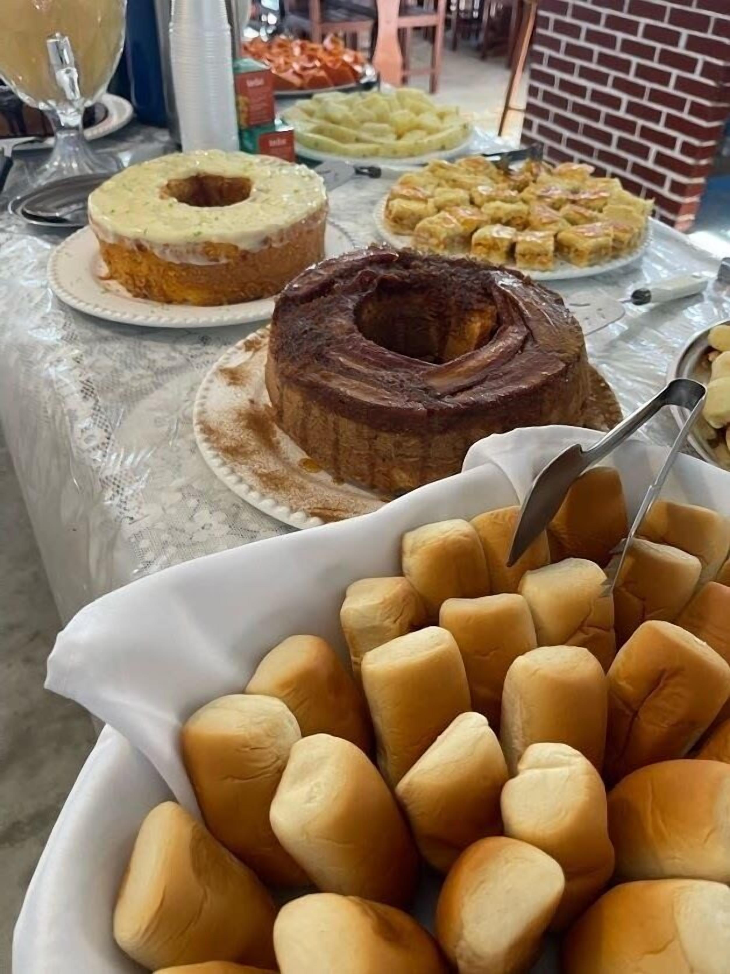 A buffet table with various baked goods including a bundt cake, a chocolate bundt cake, and rolls.