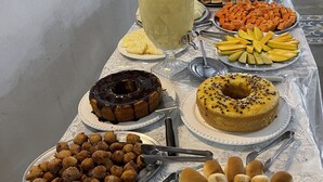 A buffet table with various food items including a large pitcher of lemonade, plates of fruits, cakes, and pastries.