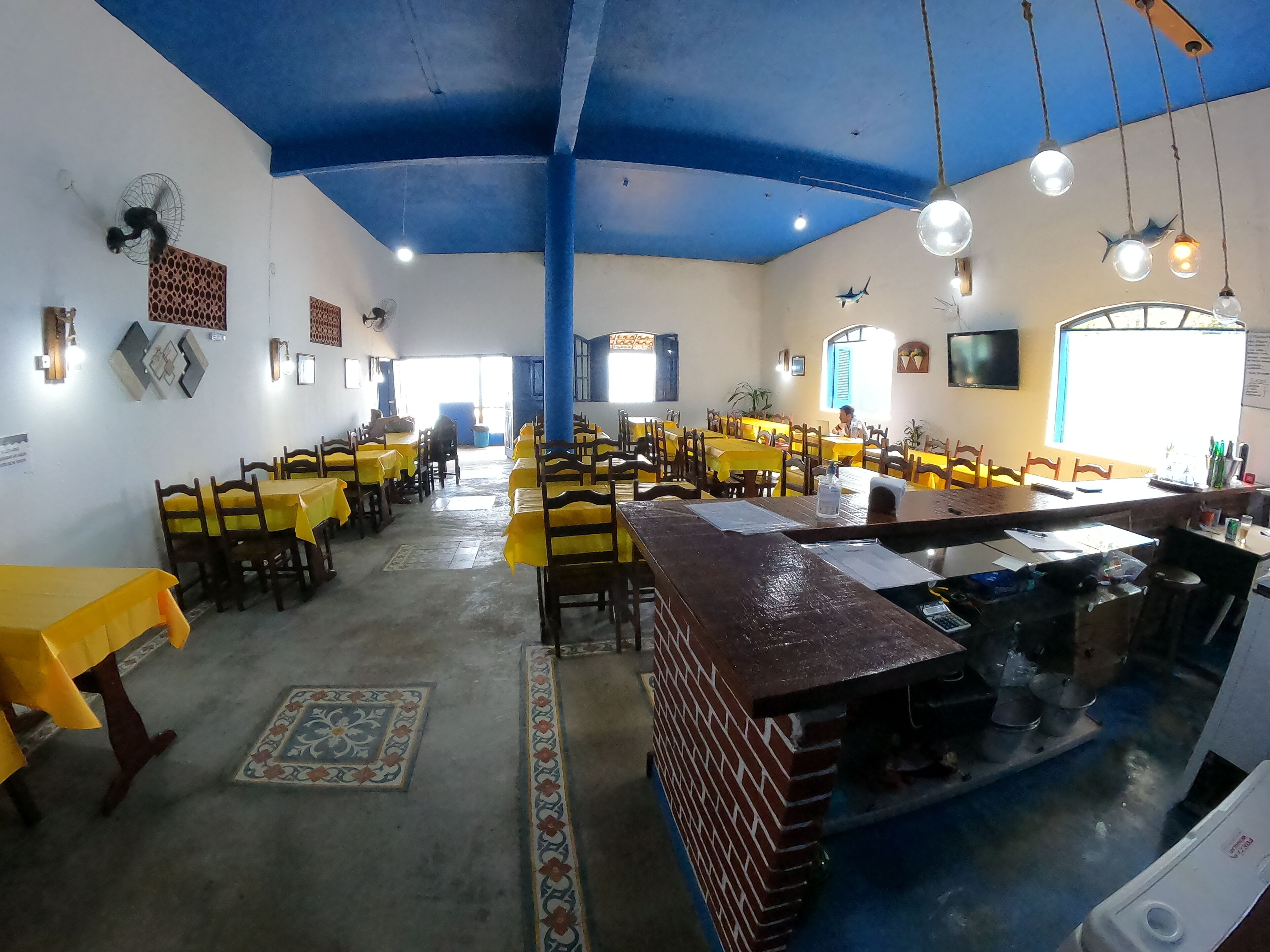Un restaurant avec des nappes jaunes, des chaises en bois, un plafond bleu et un comptoir en briques.