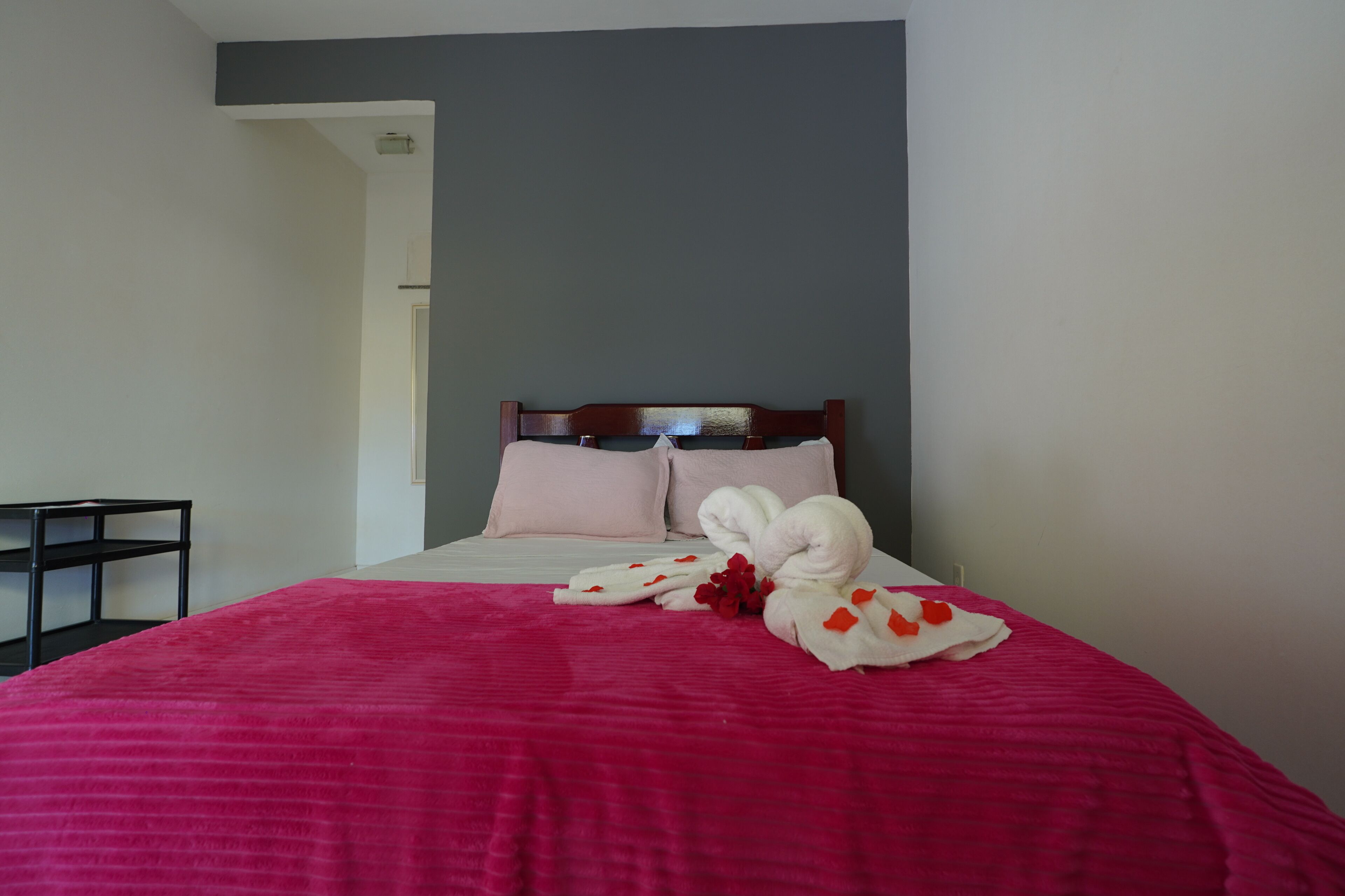 A neatly made bed with a pink bedspread, two pillows, and a set of white towels with red flowers.