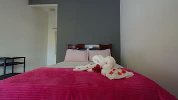 A neatly made bed with a pink bedspread, two pillows, and a set of white towels with red flowers.