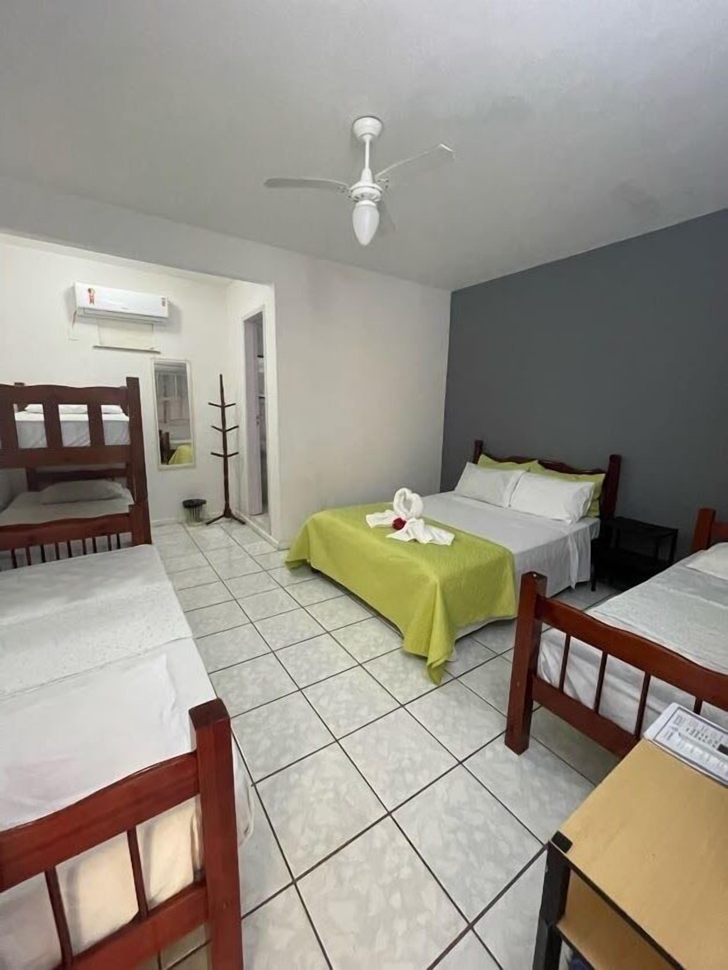 Une chambre d’hôtel avec deux lits, un ventilateur de plafond, une petite table et une fenêtre.