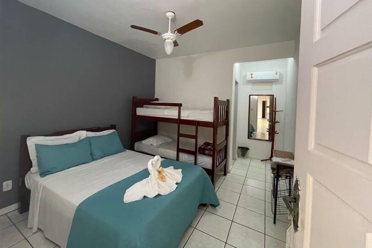 A room with a bed, a bunk bed, a ceiling fan, a desk, and a chair.