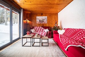 A cozy room with a red sofa, a wooden ceiling, a large window, and a Christmas tree.
