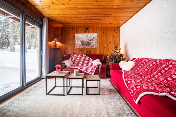 A cozy room with a red sofa, a wooden ceiling, a large window, and a Christmas tree.