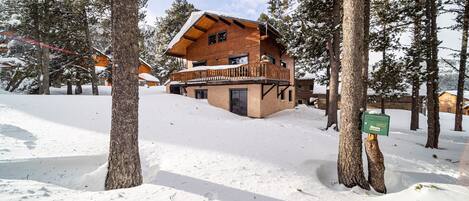A wooden cabin with a balcony, surrounded by snow-covered trees.