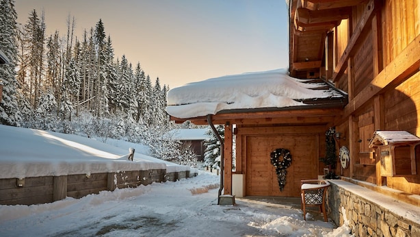 A wooden cabin with a snow-covered roof and a stone wall entrance.