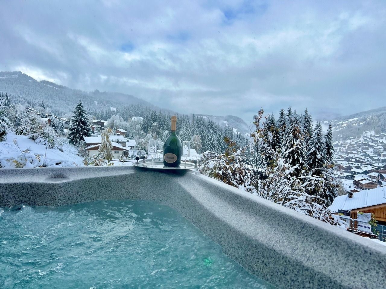Ett spaområde med ett bubbelbad, omgivet av snötäckta träd och en bergig kuliss.