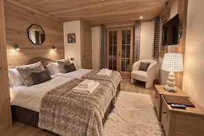 A cozy bedroom with two beds, a chair, a TV, and a lamp.