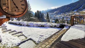A clock with Roman numerals, a wooden deck, and a snowy landscape with a town in the background.