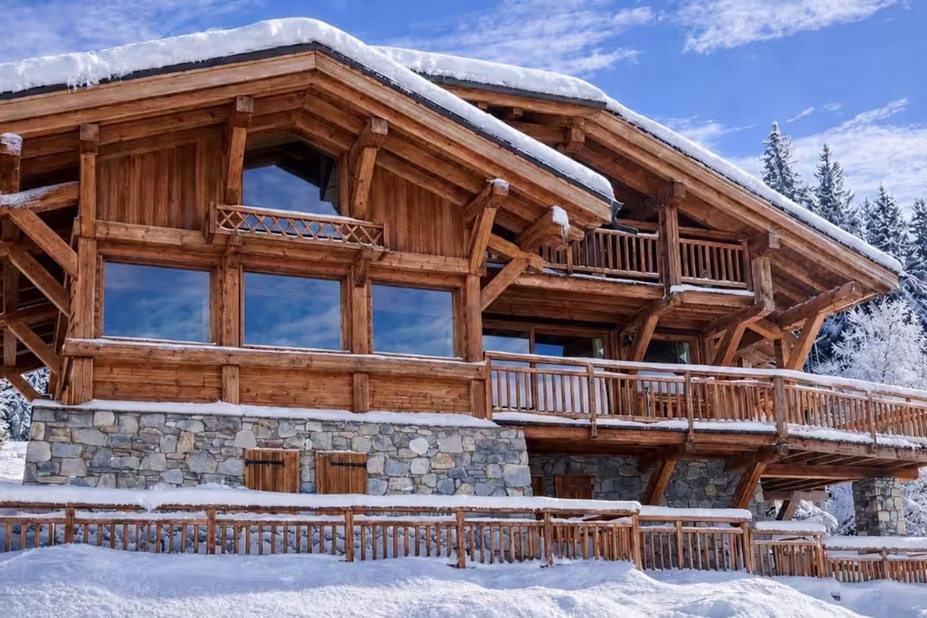 A wooden chalet with a stone foundation, large windows, and a balcony.