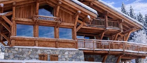 A wooden chalet with a stone foundation, large windows, and a balcony.