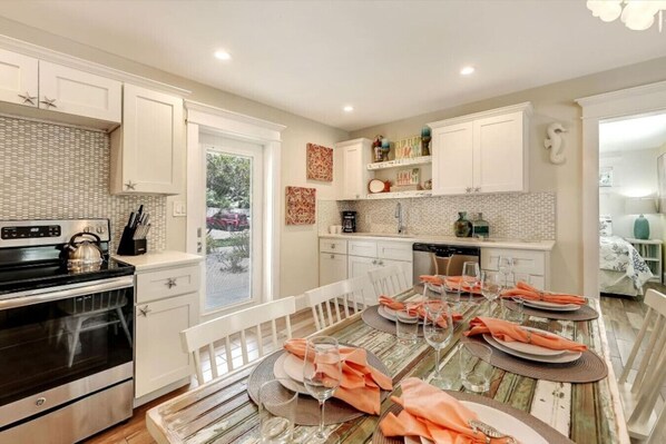 A modern kitchen with white cabinetry, a dining table set for six, and a large window.