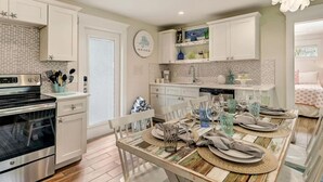 Une cuisine moderne avec des meubles blancs, un coin repas doté d’une table en bois pour quatre personnes et un îlot de cuisine bien visible.